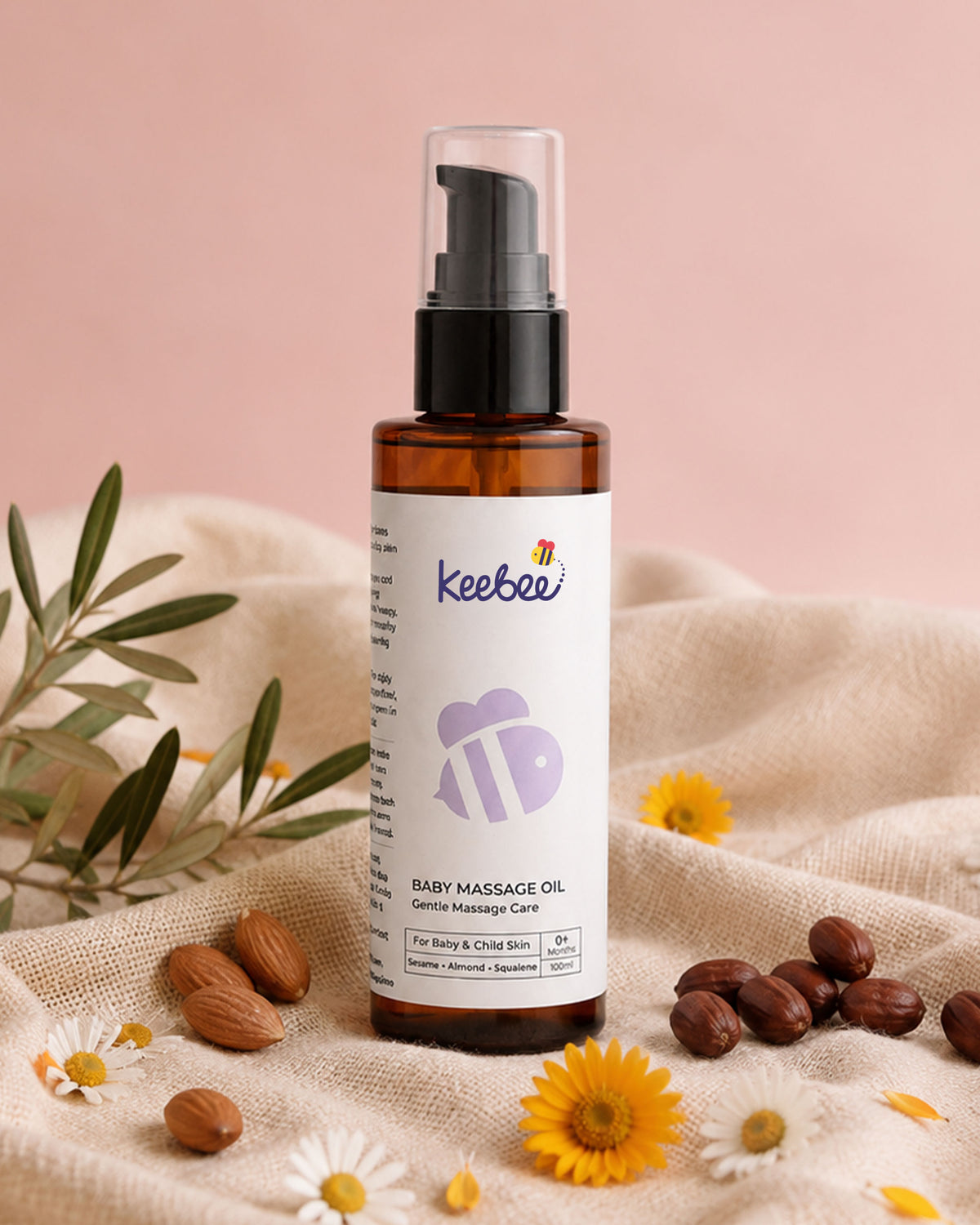 A bottle of Keebee Baby Massage Oil in an amber glass bottle with a black pump and clear cap, set on a beige fabric with almonds, daisies, and yellow flowers against a soft pink background.